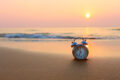 Vintage alarm clock on a beach at sunset.