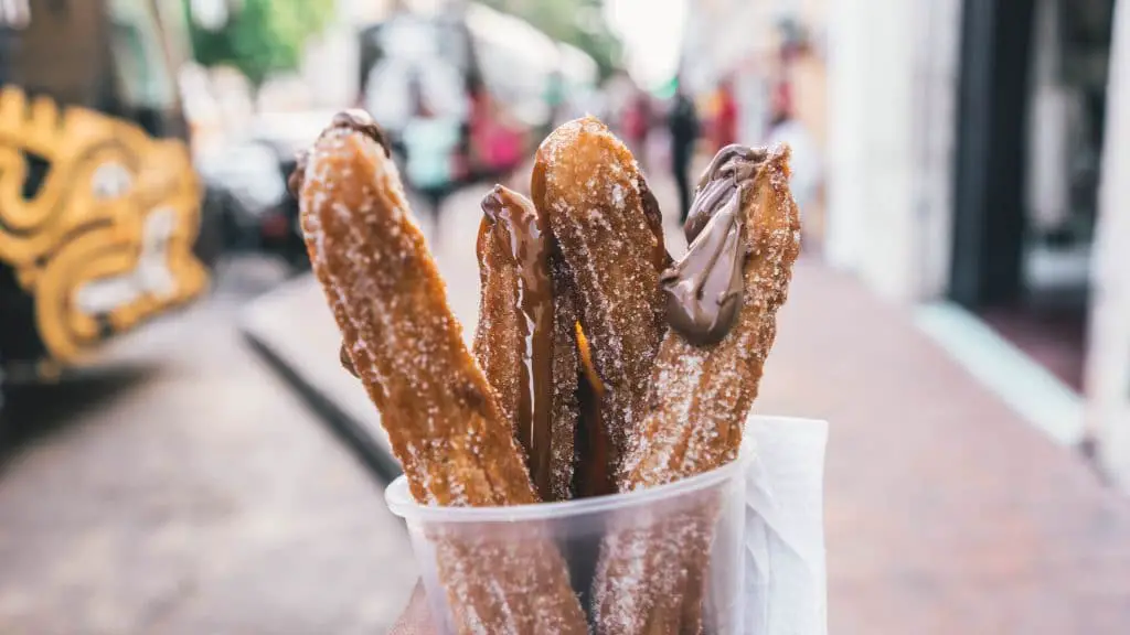 A cup full of sugary churros and chocolate sauce.