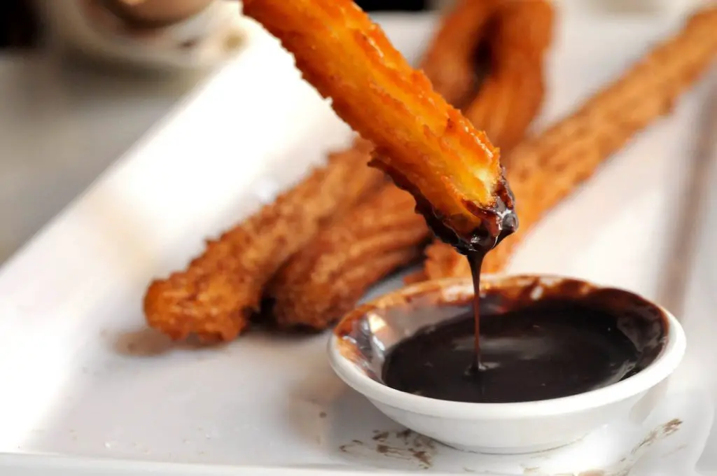 Plate of fresh churros with small bowl of warm chocolate sauce. 