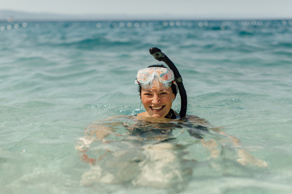 Woman all smiles as she takes a brief break from snorkeling in clear blue ocean water, like Cozumel's.