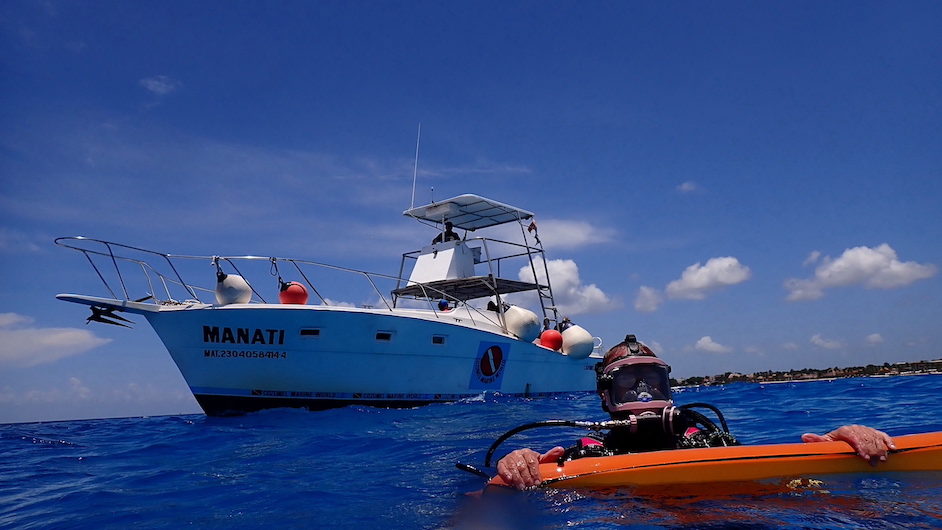Cozumel diver in foreground with bright orange marker buoy, and boat coming to pick him up.