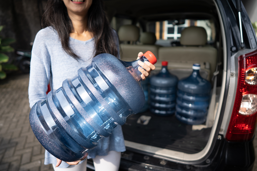 Big clear blue water jug held by woman near a car. 