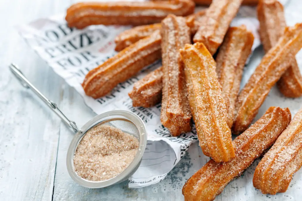 Order of about a dozen churros on newspaper and dusted with cinnamon and sugar.