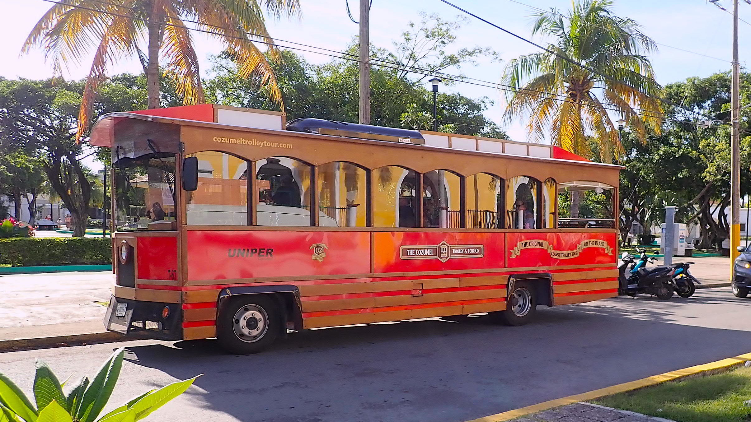 Cozumel red trolley tour vehicle riding past the Corpus Christi church.