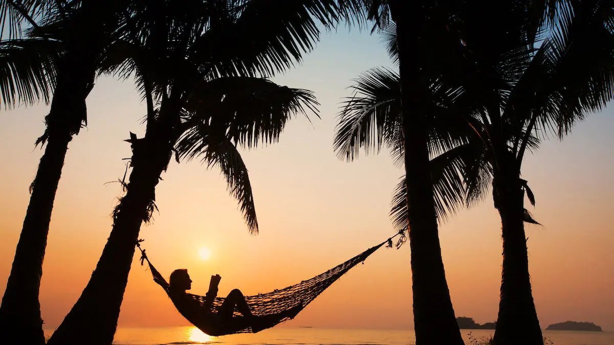 Silhouette of woman in a hammock relaxing during a stunning orange sunset.
