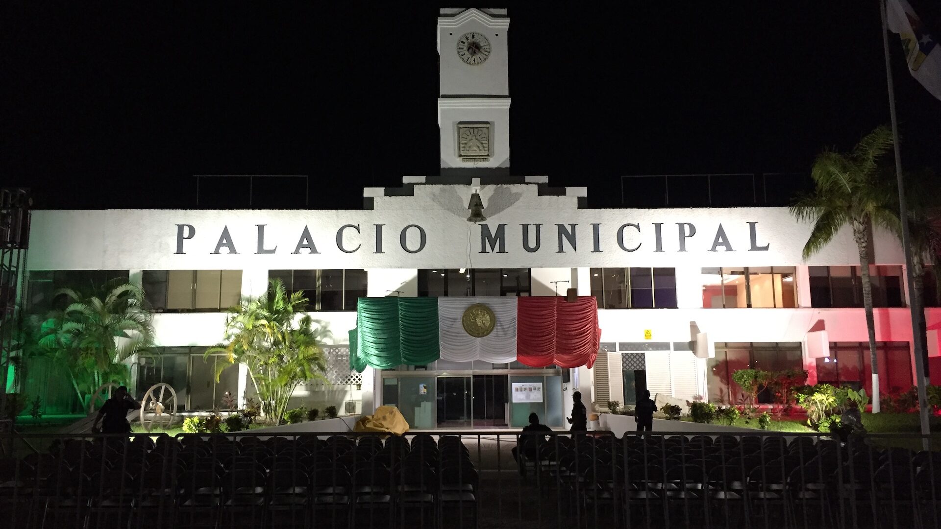 Front view of the Cozumel Palacio city hall at night with large Mexican flag on facade.