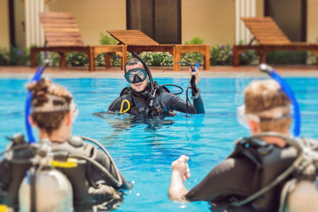 A diving instructor in the pool with several adult scuba diving students.