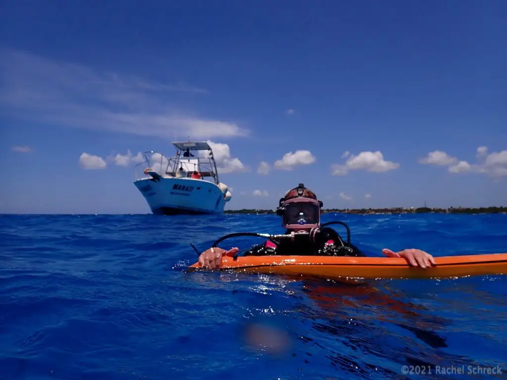 Diver in Cozumel with an orange surface marker bouy in deep blue water with dive boat in the background