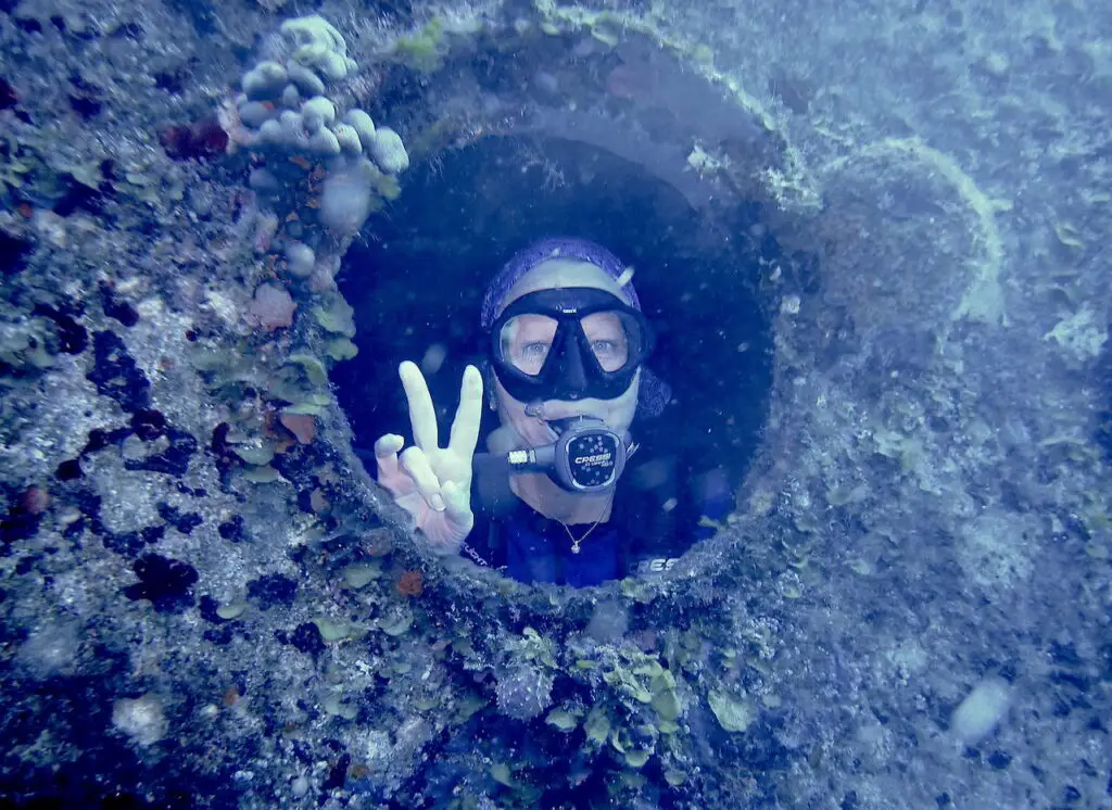 Female diver posing in the porthole of the C-53 shipwreck dive site in Cozumel. 