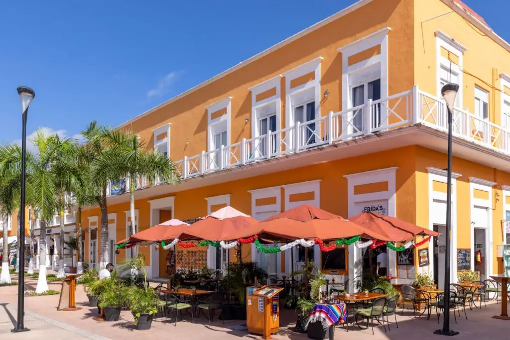 Shopping in Cozumel's Plaza del Sol which is within the central Parque Benito Juarez, image showing brightly colored colonial era architecture.