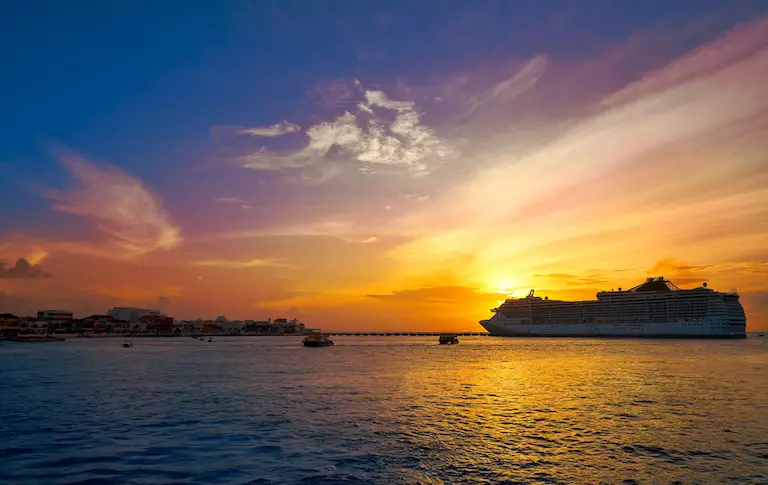 Vibrant sunset in Cozumel with pier and large cruise ship silhouetted in the foreground.