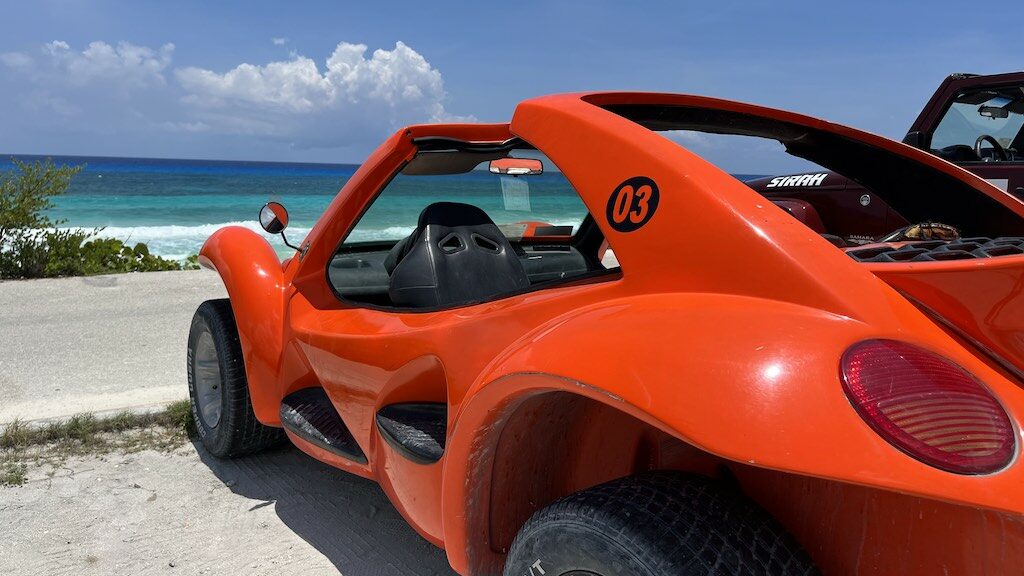 Author's image of bright orange dune buggy vehicle parked on the side of the coastal road in Cozumel, with bright blue ocean in the background. 