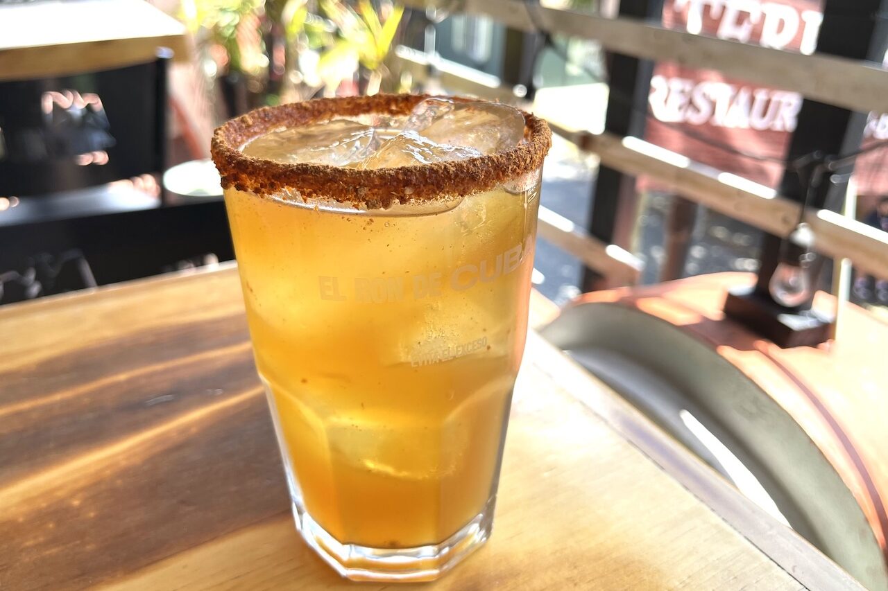 Glass of tepache on ice with chili-spiced rim, overlooking a Mexican street scene. 