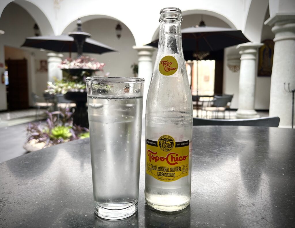 Image of cold bottle of Topo Chico club soda and glass of ice in hotel lobby in Mexico. By author. 